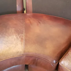A side-by-side comparison of a brown leather sofa cushion, showing scuffed and worn leather on the left and restored, smooth leather on the right.